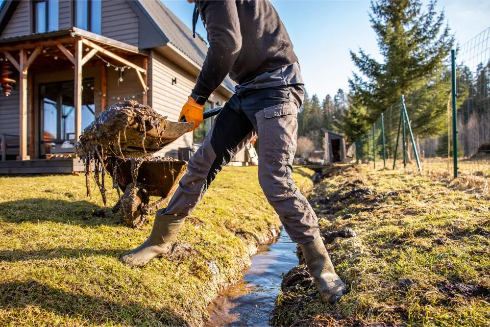 How Residential Land Clearing Works: Cost, Steps & Tips 4 man protective gear tirelessly working dredge muddy trench with shovel wheelbarrow backyard early spring residential land clearing